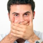 A Man Looking At Camera By Closing His Mouth With His Hand Representing Sign Language.