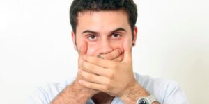 A Man Looking At Camera By Closing His Mouth With His Hand Representing Sign Language.